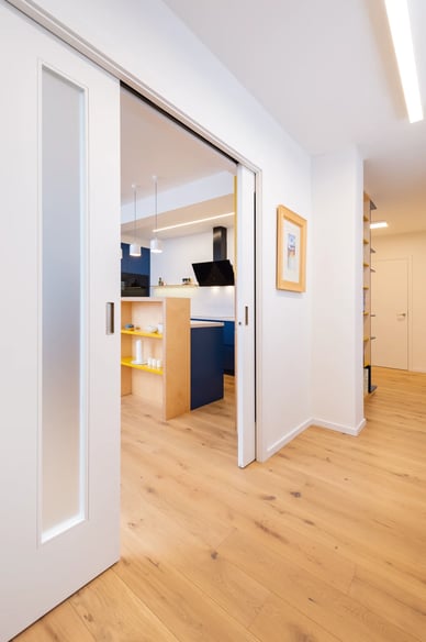 Moderní interiér s dřevěnou podlahou a posuvnými dveřmi do kuchyně.